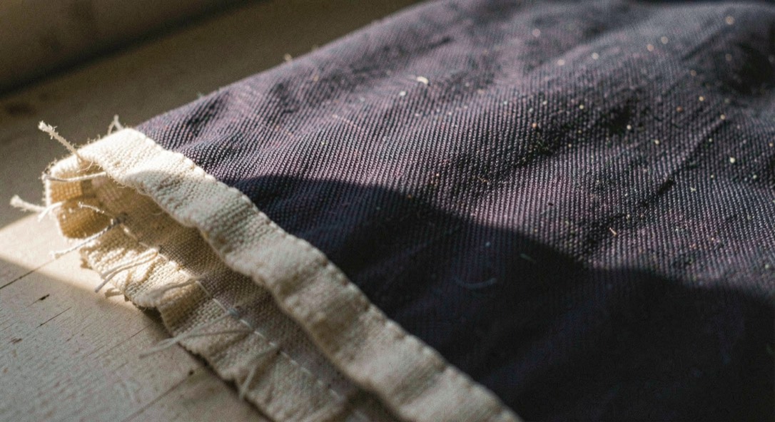 Dark indigo twill crosses an unbleached selvedge edge under raking light